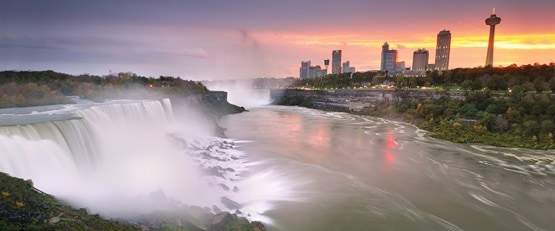 Niagara Falls at sunset with skyscrapers in the background.